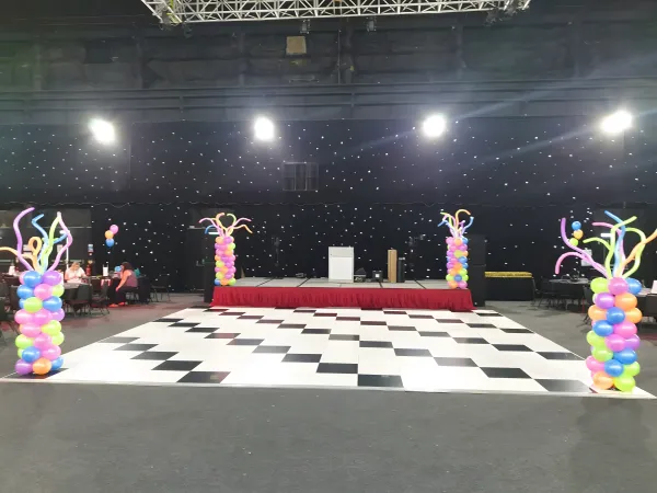 Dance floor setup with checkerboard floor and neon balloon columns